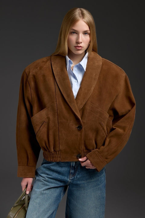 A woman wears a brown suede jacket with wide sculpted shoulders and a flattering cropped length, blending modern structure with timeless sophistication.