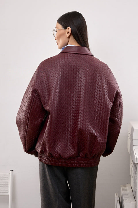 A woman in a burgundy bomber jacket featuring clean lines and side pockets, blending casual ease with contemporary sophistication.