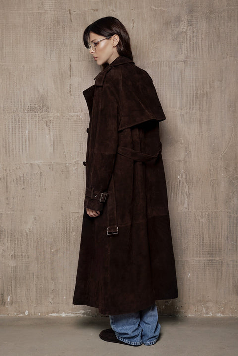 A woman dressed in a rich suede leather trench coat, showcasing a double-breasted design and a sleek, flattering cut that blends classic style with contemporary appeal.